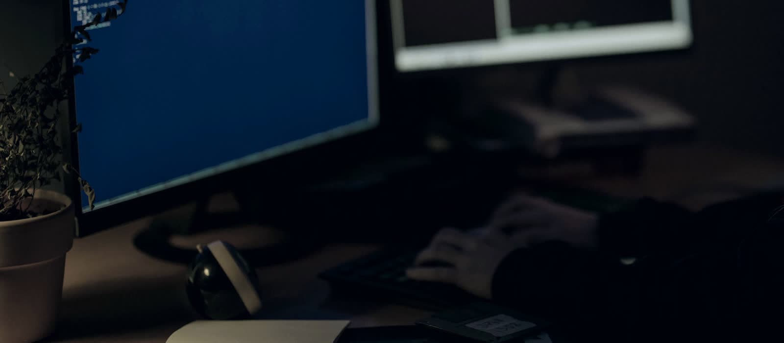 Someone typing at a desk with two monitors at night