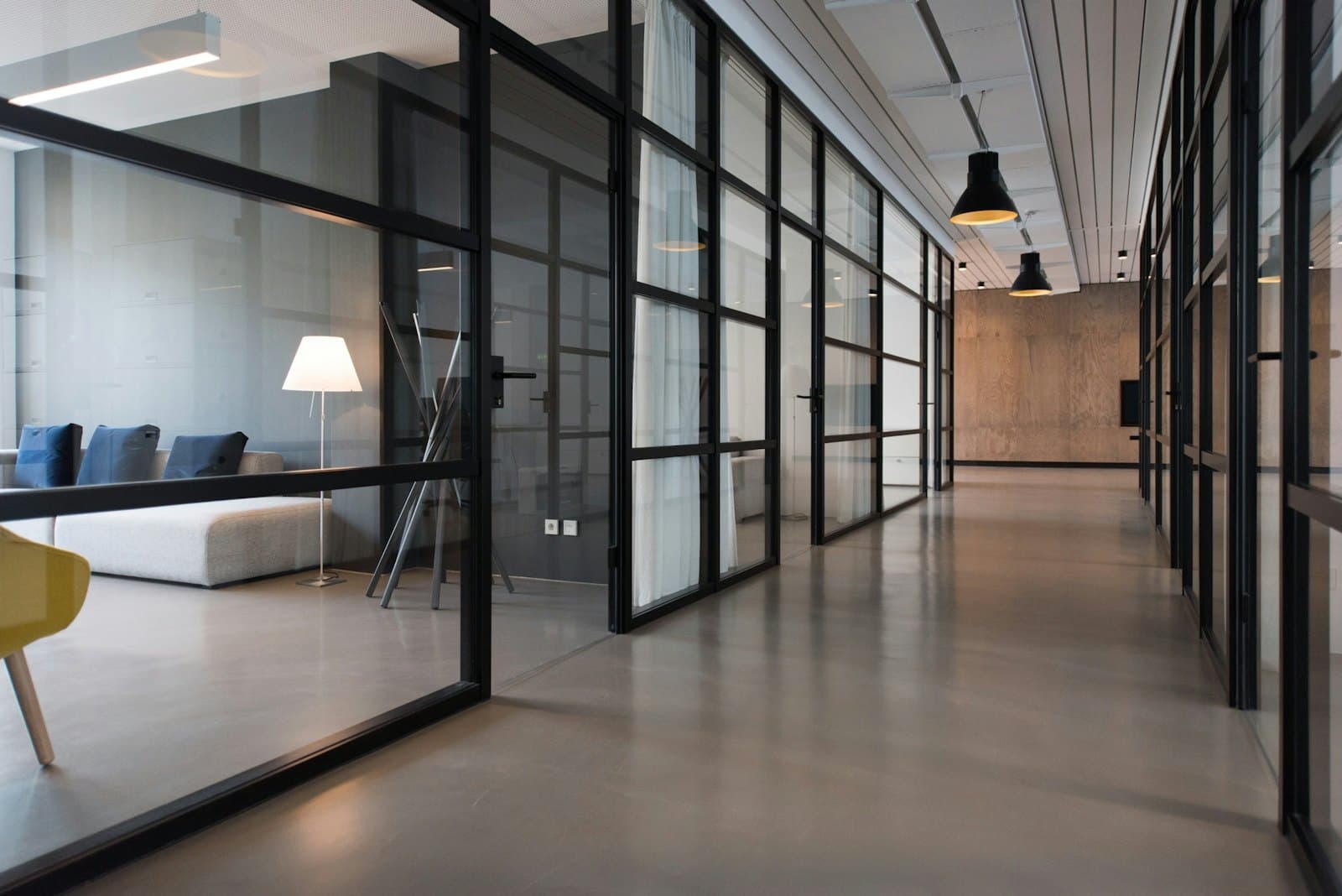A quiet office corridor with glass partitions and empty seating