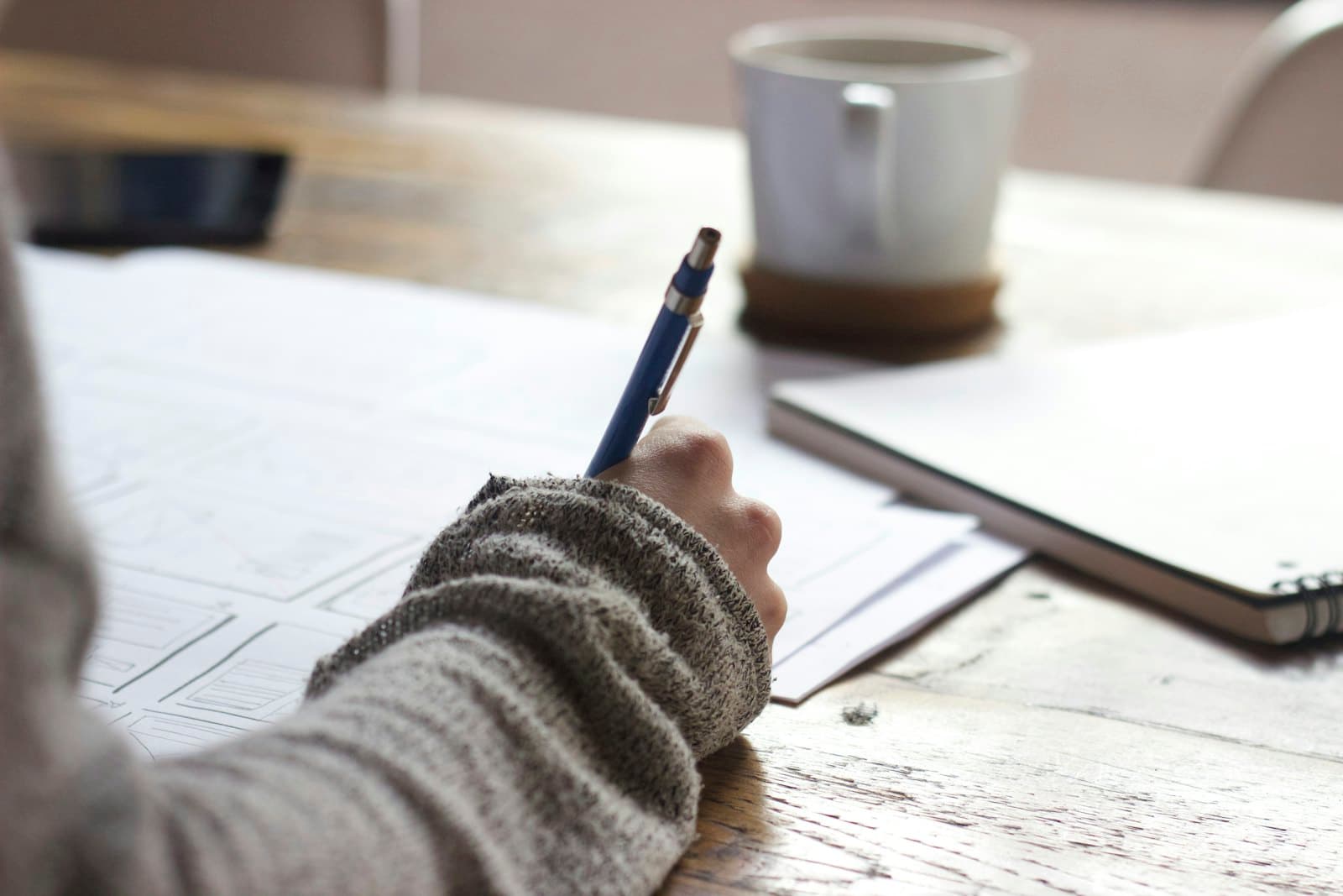 A person writing notes at a desk beside a cup of coffee