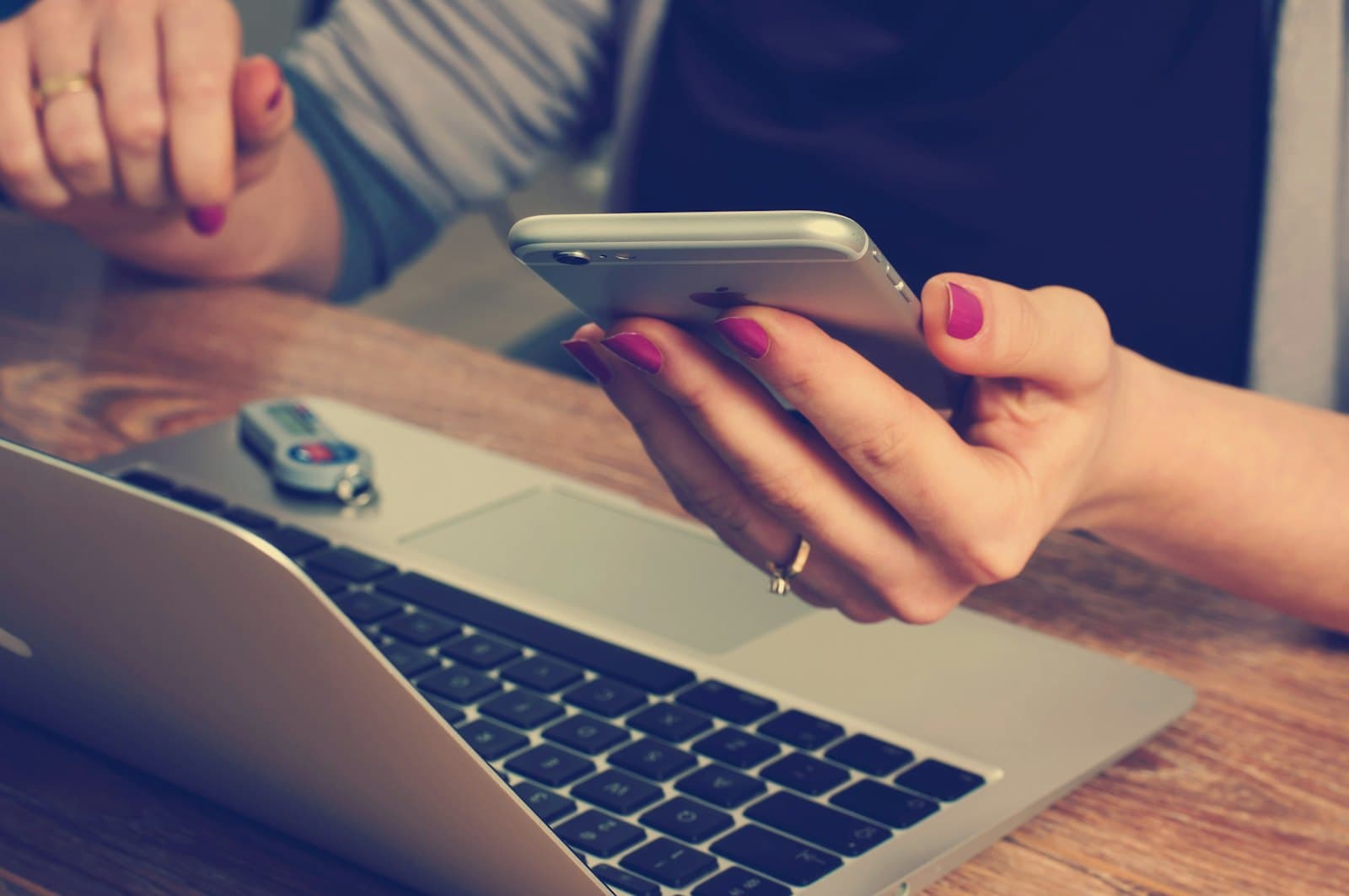 Hands holding a phone beside an open laptop