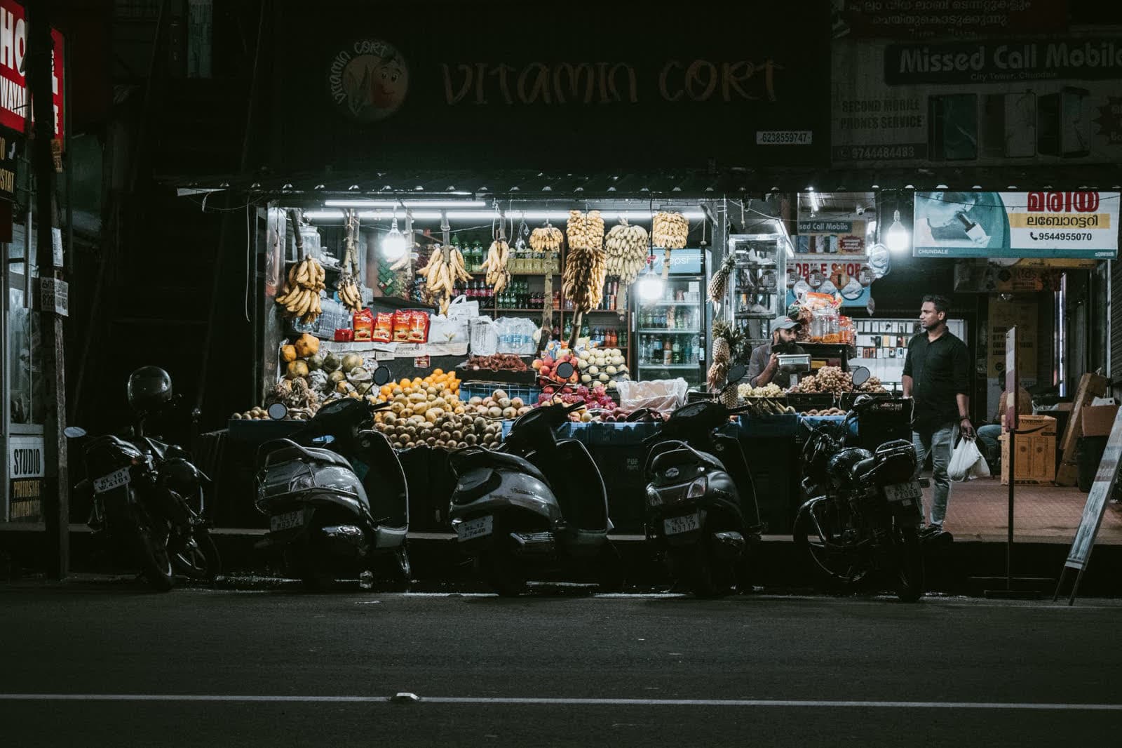 A market stall lit up at night, scooters parked outside